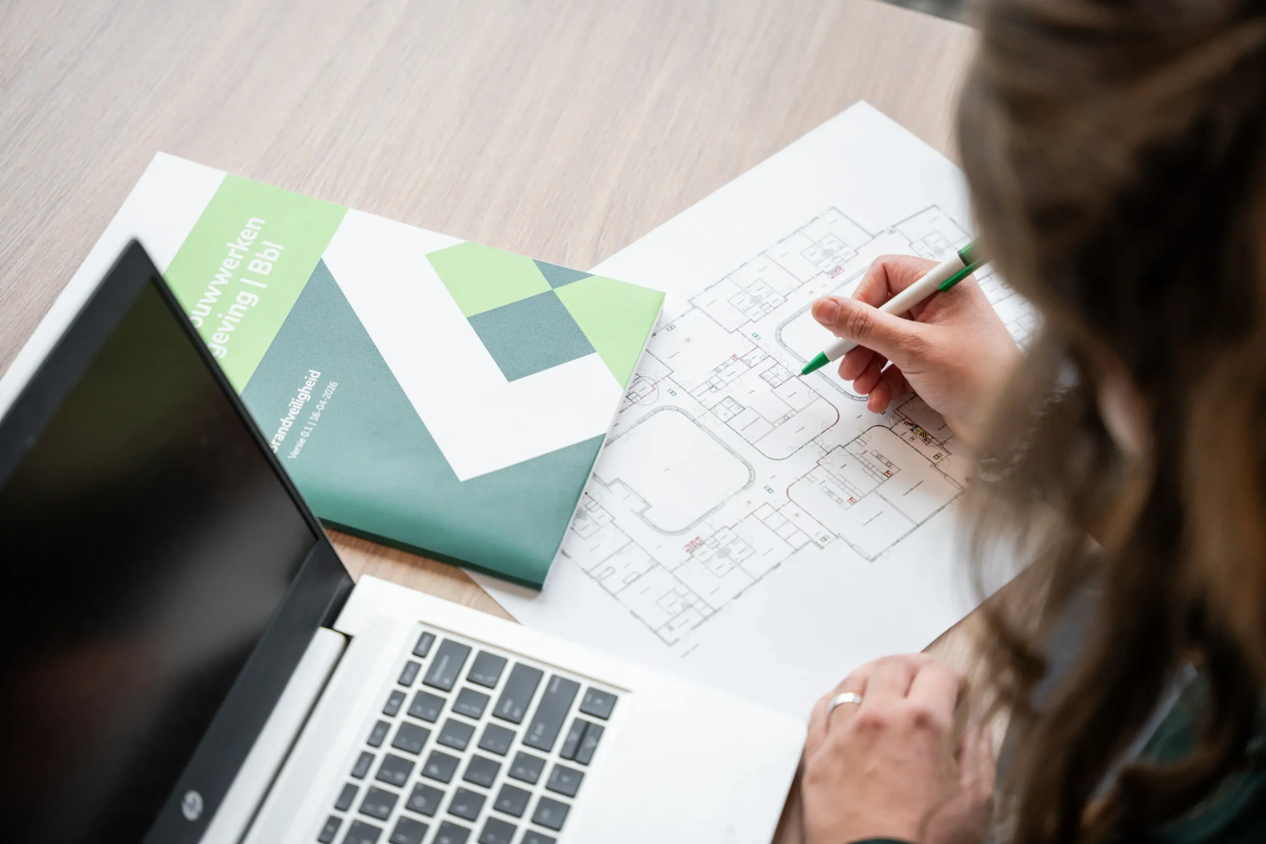 Vrouw die aantekeningen maakt op een plattegrond met een laptop naast zich